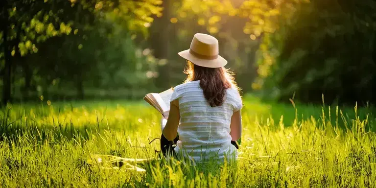 Eine junge Frau sitzt in einem Park und liest ein Buch