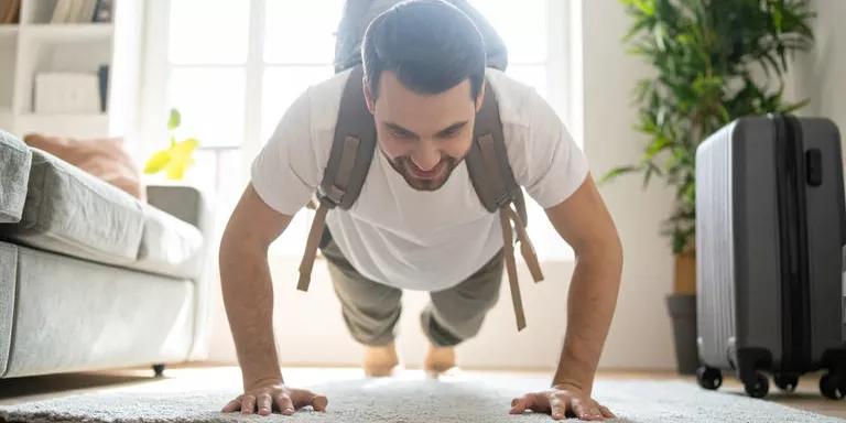 Mann trainiert mit einem Rucksack in einer hellen Ferienwohnung während seines Urlaubs.