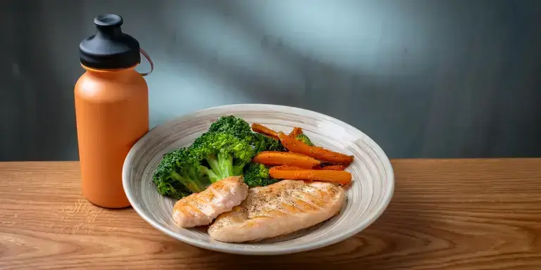 Ein gesundes Fitnessgericht mit Hühnchen, Süßkartoffeln und Brokkoli auf einem Holztisch.