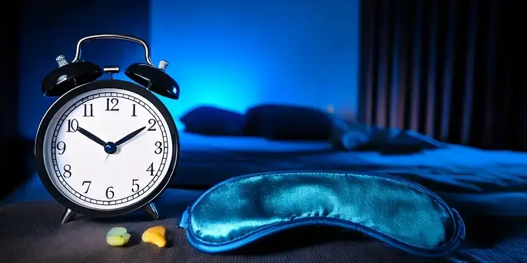 Schlafumgebung mit Wecker, Schlafmaske und Ohrstöpseln in einem abgedunkelten, bläulich beleuchteten Schlafzimmer