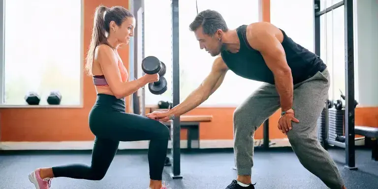 Personal Trainer zeigt einem Anfänger die richtige Übungsausführung im Fitnessstudio.