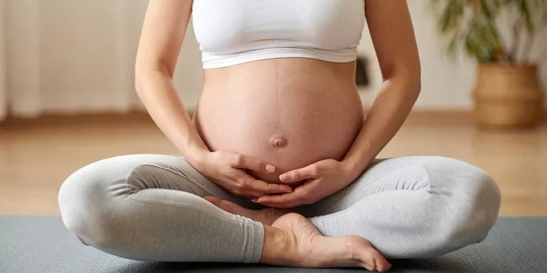 Nahaufnahme einer Schwangeren im Schneidersitz mit Händen auf dem Bauch beim Dehnen