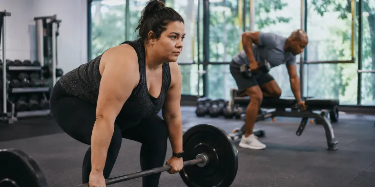 Frau beim Langhanteltraining und Mann beim Kurzhantelrudern im Fitnessstudio