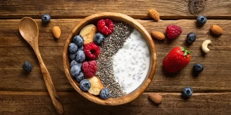 Eine gesunde Frühstücksbowl mit Kokosjoghurt, Chiasamen, Nüssen und Beeren auf einem Holztisch.