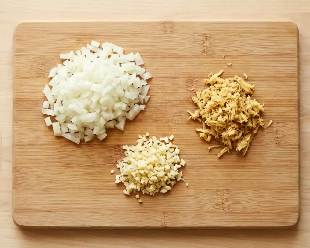 Fein gehackte Zwiebeln, Knoblauch und geriebener Ingwer auf Schneidebrett von oben