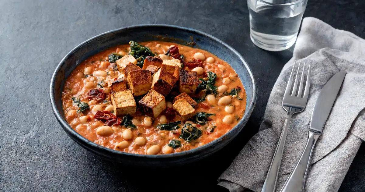 Cremige Cannellini-Bohnen mit Spinat, Tomaten und knusprig gebratenem Räuchertofu in einer dunklen Keramikschale.