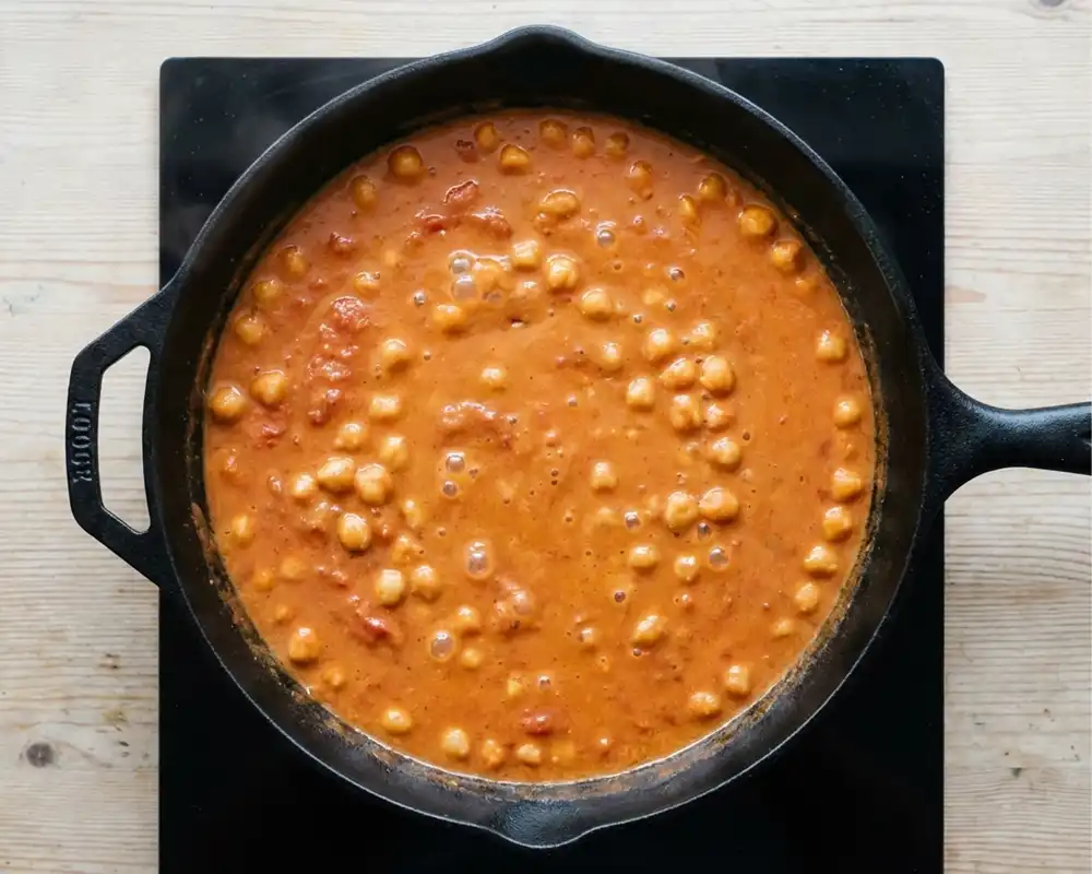 Kokos-Tomaten-Sauce mit Kichererbsen köchelt in schwarzer Pfanne – Schritt 2 Thai Kabeljau Curry