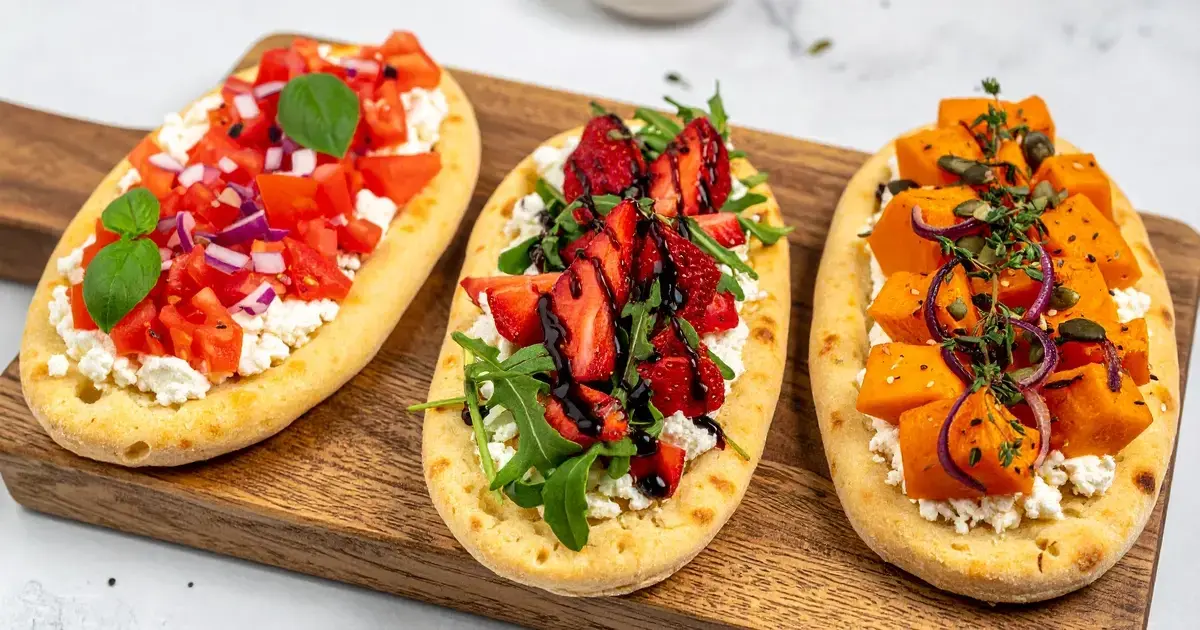 Drei Flatbreads auf Holzbrett: Bruschetta mit Tomaten und Basilikum, sommerliche Variante mit Erdbeeren und Balsamico, herbstliche Variante mit Kürbis und Thymian