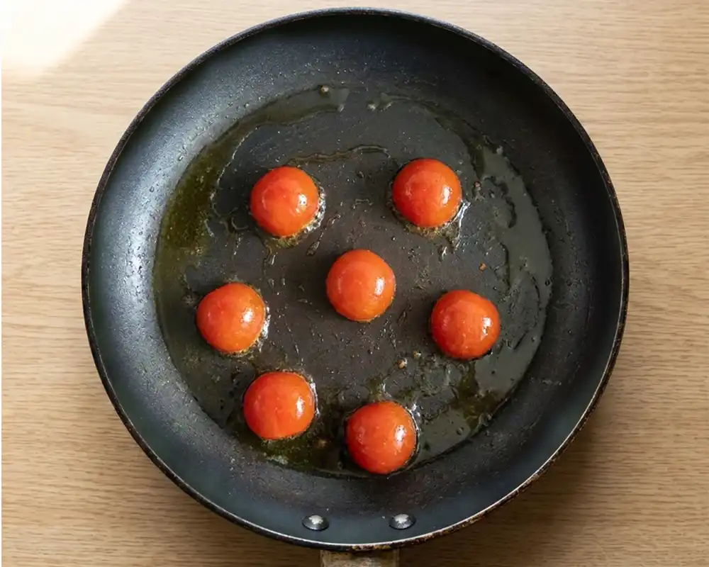 Angebratene Cocktailtomaten in beschichteter Pfanne für grünes Basilikum-Omelette von oben fotografiert