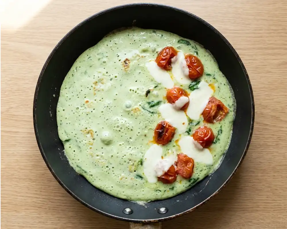 Grünes Basilikum-Omelette mit schmelzendem Mozzarella und Tomaten in Pfanne von oben fotografiert