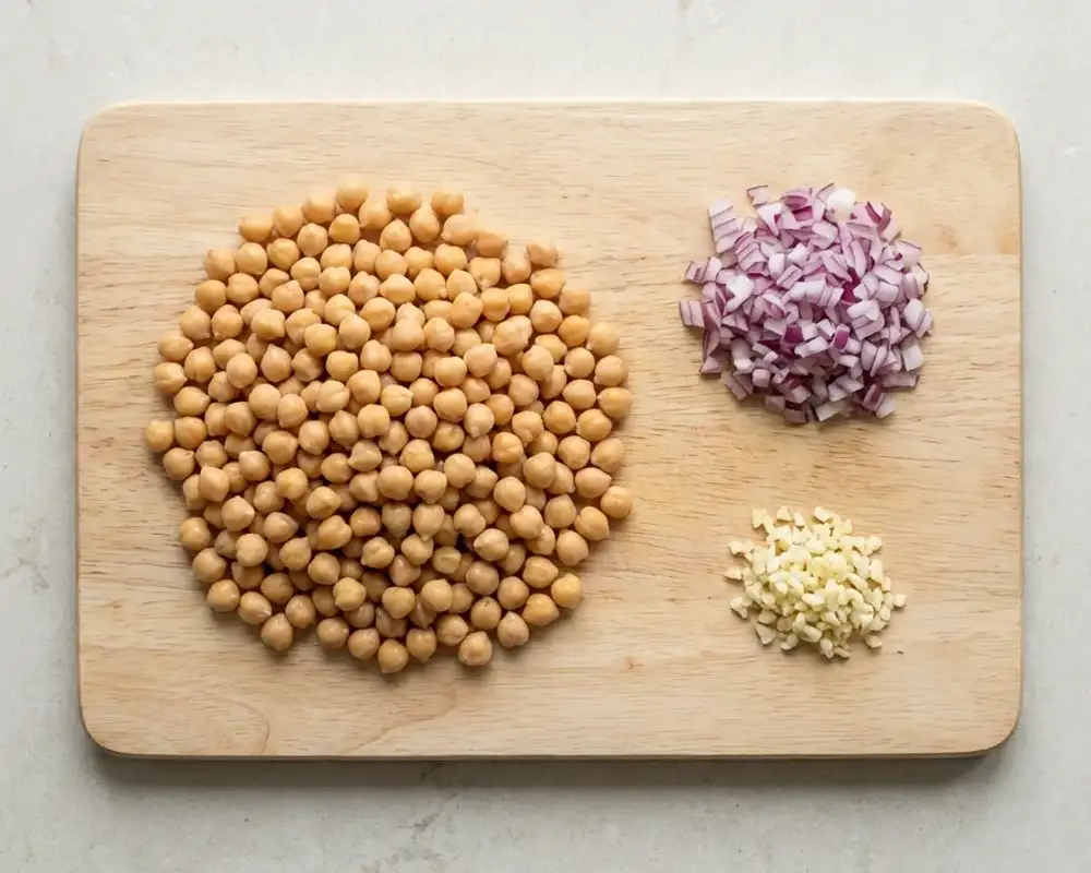 Vorbereitete Zutaten für eine High-Protein-Kichererbsen-Pfanne mit fein gewürfelter Zwiebel, gehacktem Knoblauch und abgetropften Kichererbsen in cleanem Top-Down-Stil