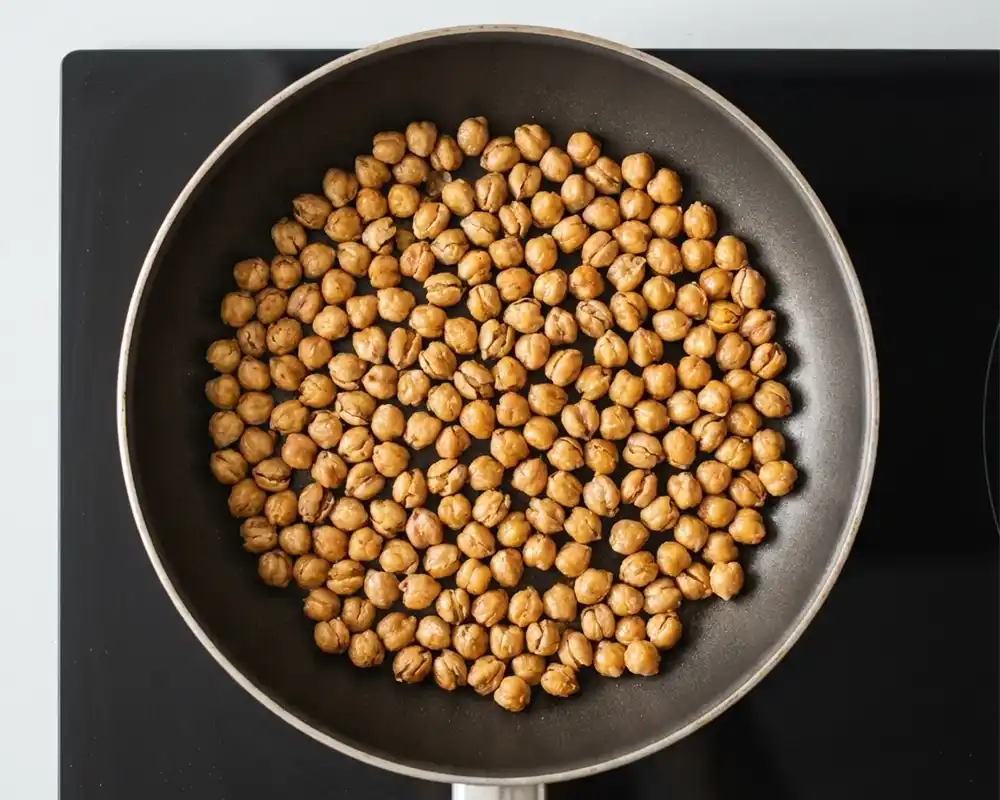 Knusprig geröstete Kichererbsen in einer Pfanne auf dem Herd von oben fotografiert, goldbraun und leicht aufgeplatzt für intensive Röstaromen