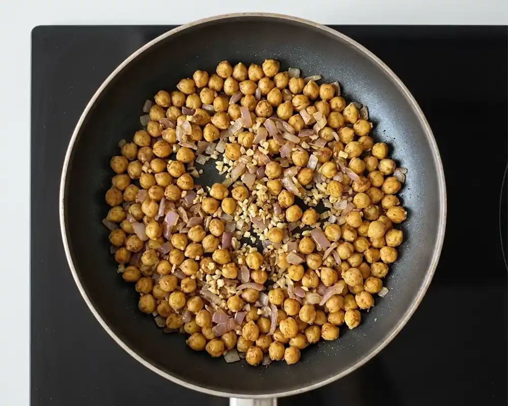 Geröstete Kichererbsen mit glasiger Zwiebel, Knoblauch und Gewürzen in der Pfanne von oben, würzige Basis für eine schnelle High-Protein-Pfanne