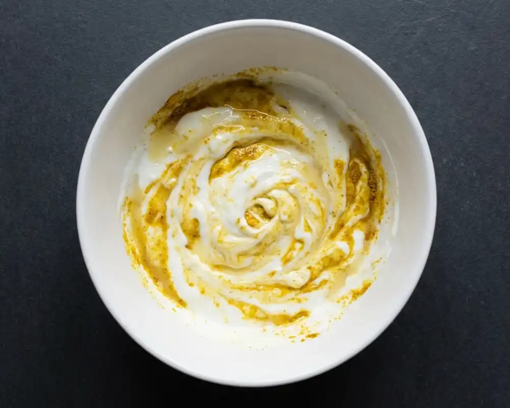 Skyr-Dip mit Currypulver und Zitronensaft beim Anrühren in weißer Schüssel