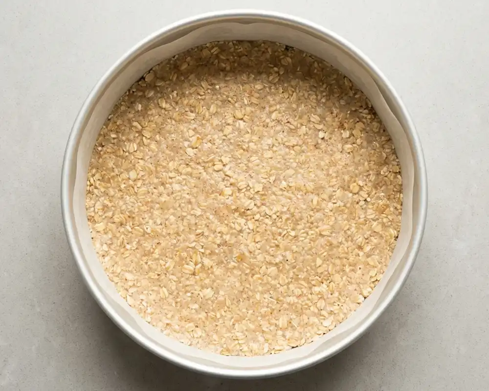 Gleichmäßig in eine 18 cm Springform gedrückter Hafer-Mandel-Boden für Protein-Käsekuchen von oben fotografiert