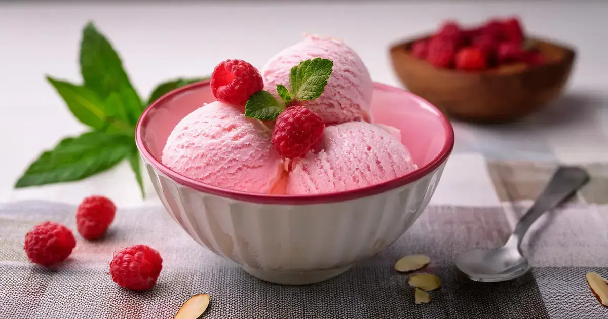 Schale mit cremigem Mandel-Himbeer-Eis, garniert mit frischen Himbeeren und Mandelblättchen.