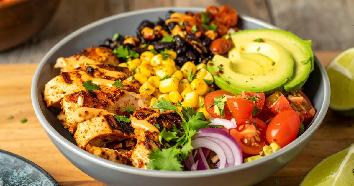 Mexikanische Bowl mit Hähnchen, schwarzem Bohnen, Mais, Avocado und Chipotle-Dressing in einer Schale serviert.