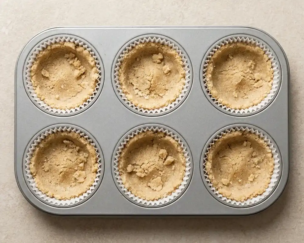 Mandelboden in Muffinförmchen vor dem Backen gleichmäßig verteilt