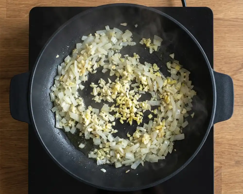 Glasig gedünstete Zwiebeln, Knoblauch und Ingwer in schwarzer Pfanne von oben