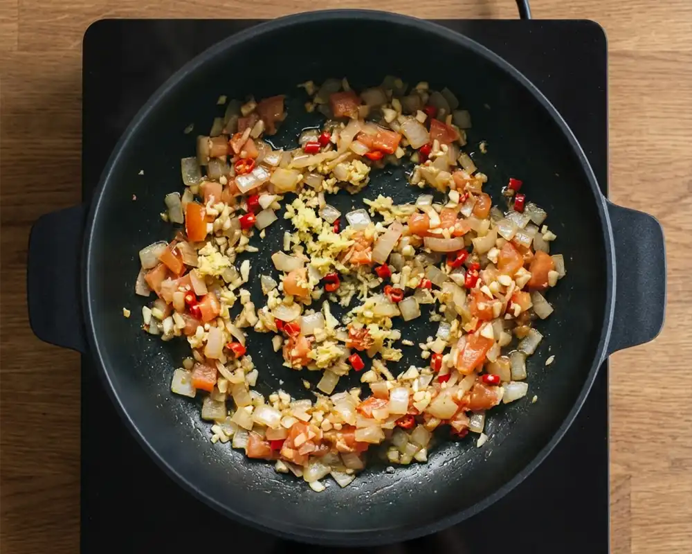 Gedünstete Tomaten und Chili mit Zwiebelmischung in Pfanne von oben