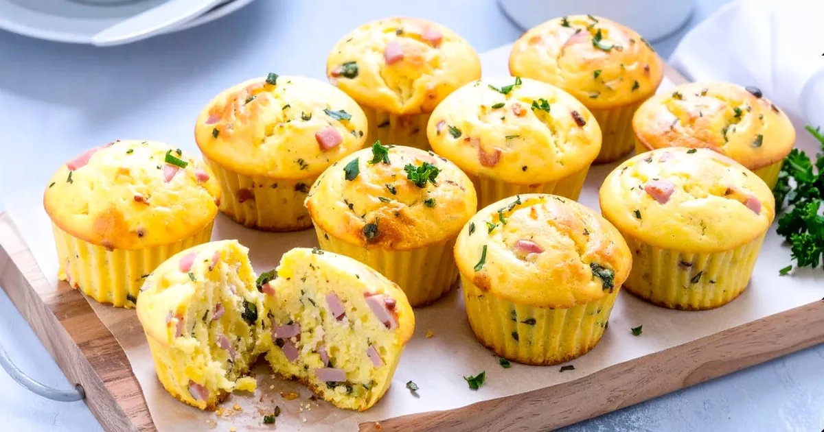 Acht fettarme Protein-Muffins mit Hüttenkäse, Schinken und Kräutern auf einem Holzbrett, einer angeschnitten