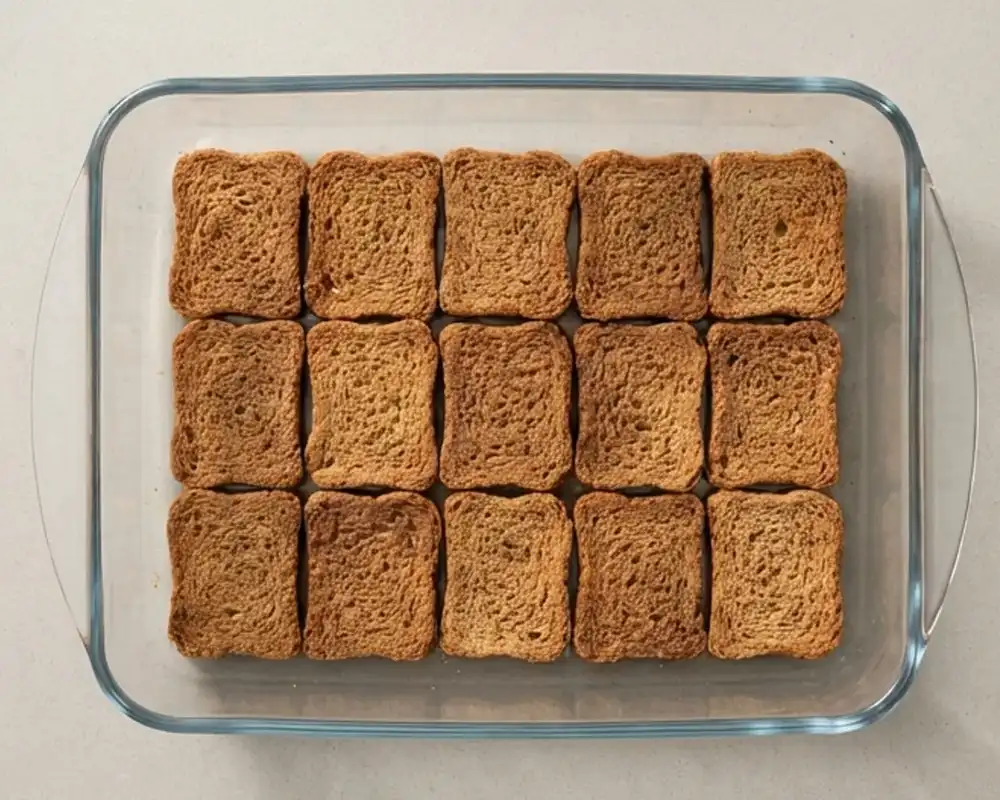 Erste Schicht in Kaffee getränkter Zwieback für Protein-Tiramisu in Glasform von oben