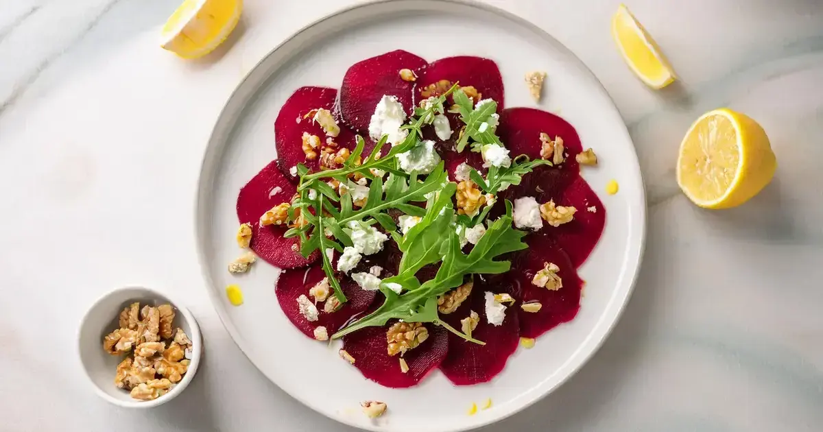 Rote-Bete-Carpaccio mit Walnüssen, Rucola und Feta, ansprechend auf einem weißen Teller angerichtet.