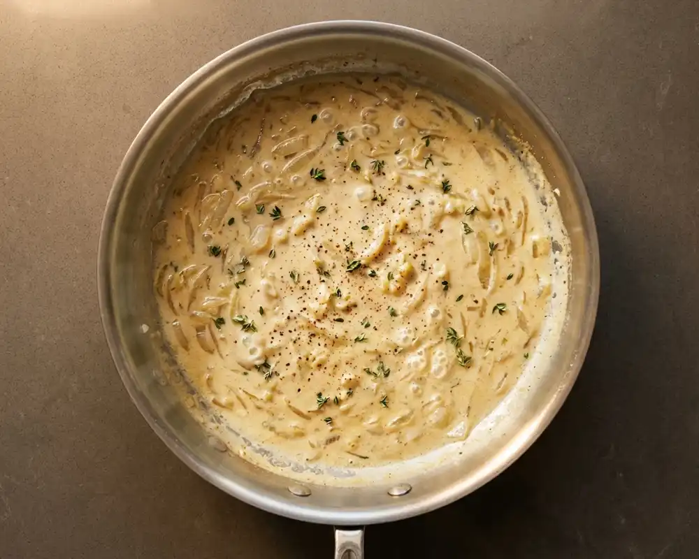 Cremige Sahne-Milch-Sauce mit Zwiebeln und Thymian in der Pfanne