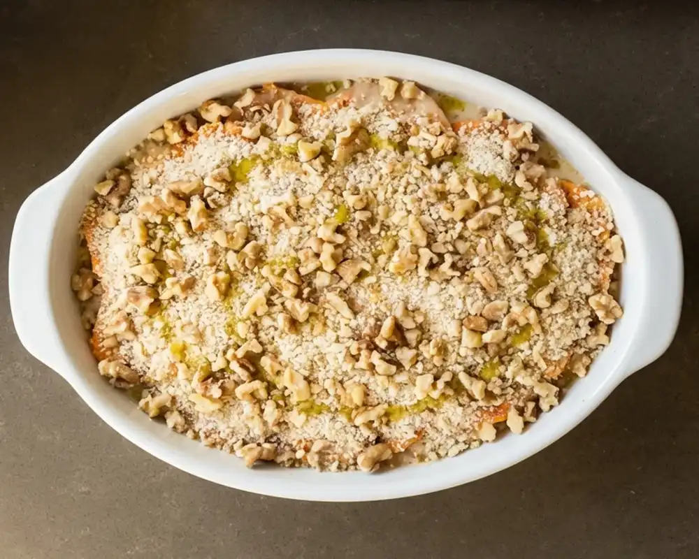 Walnuss-Semmelbrösel-Topping roh auf Süßkartoffel-Gratin verteilt