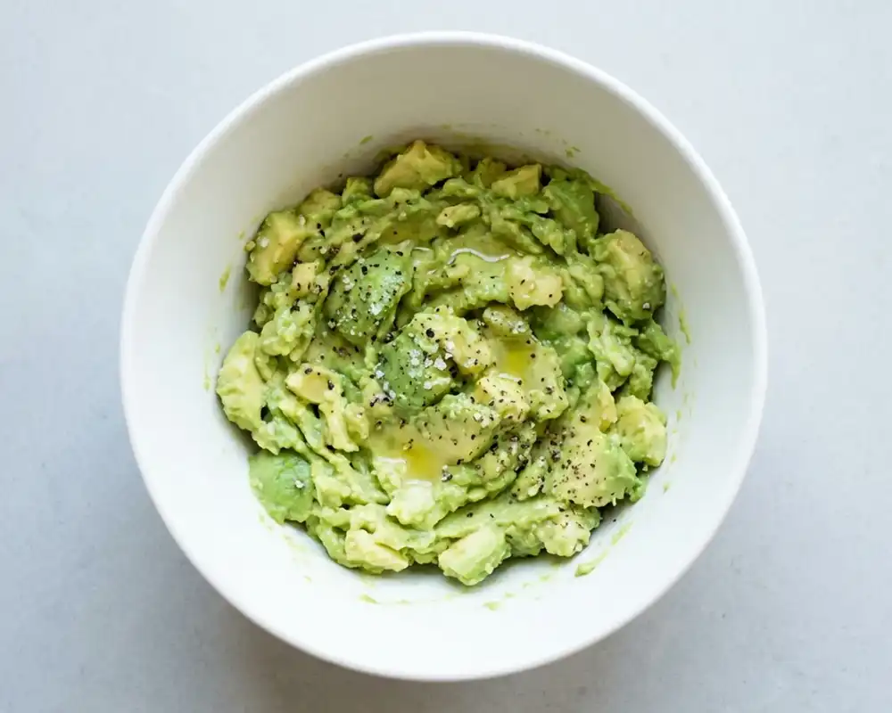 Grob zerdrückte Avocado mit Zitronensaft in weißer Schüssel