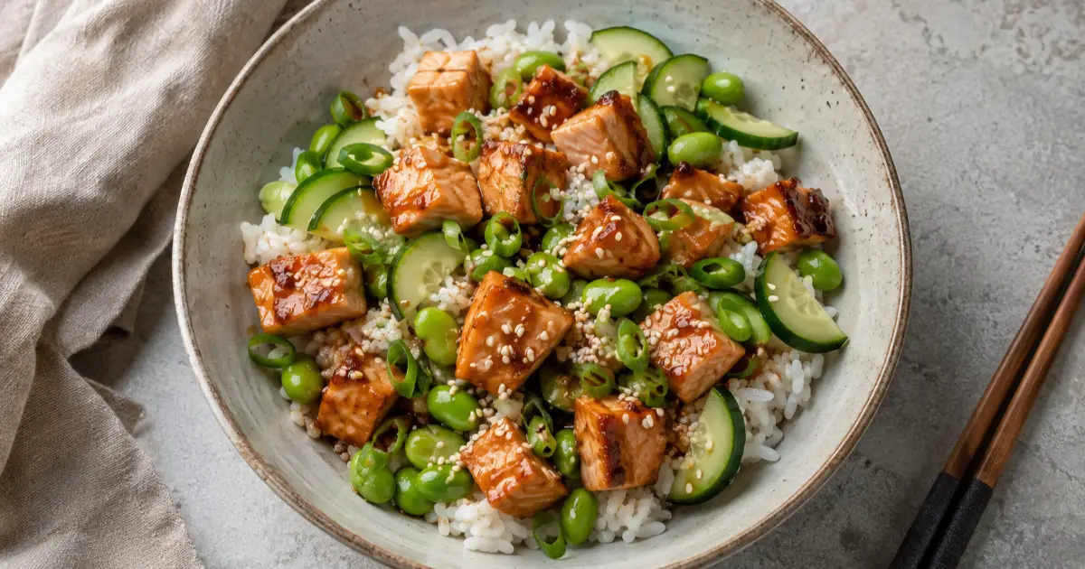 Teriyaki-Lachs-Bowl mit Jasminreis, Edamame, Gurke, Frühlingszwiebeln und Sesam.