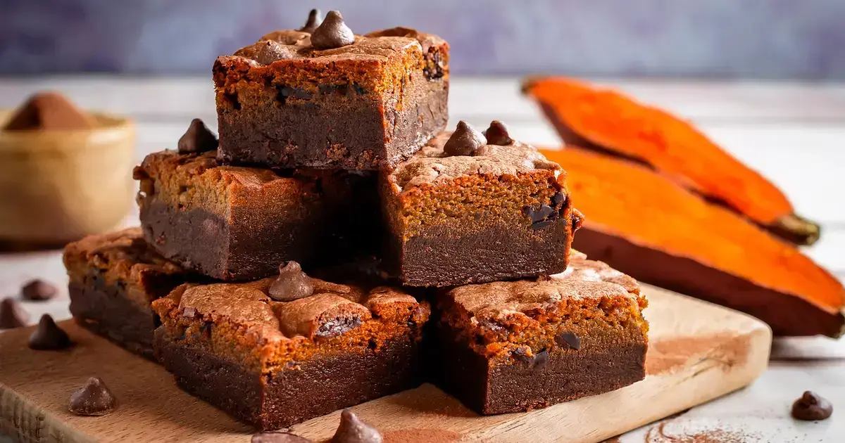 Saftige vegane Brownies aus Süßkartoffeln mit dunkler Schokolade, auf einem Holzbrett serviert.