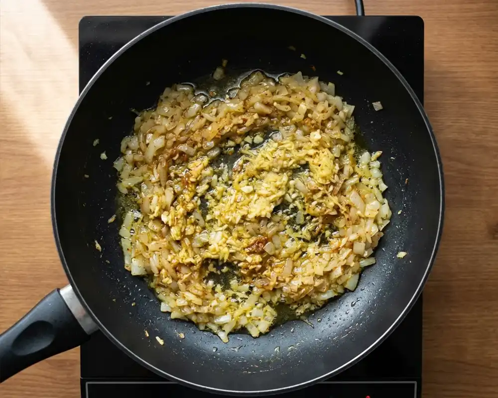 Zwiebel Knoblauch und Ingwer mit Gewürzen in Pfanne von oben für vegane Curry Basis