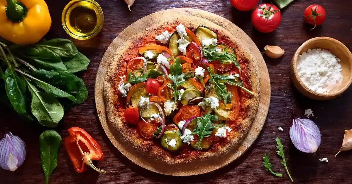 Eine frisch gebackene Vollkornpizza, belegt mit Tomatensauce, roter Paprika, Zucchini, roten Zwiebeln und zerbröckeltem Ziegenkäse, garniert mit frischem Rucola.